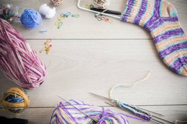 Colored threads, knitting needles and other items for hand knitting, on a light wooden table .
