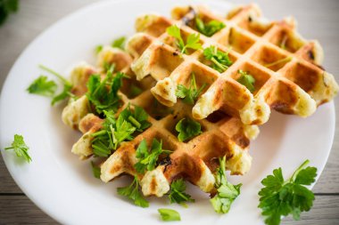 fried Belgian vegetable waffles with spices and herbs, in a plate on a light wooden table.