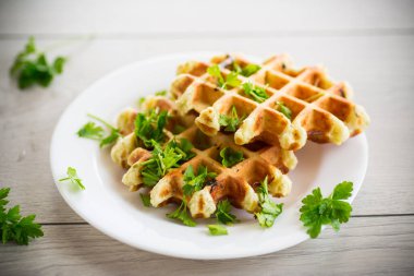 fried Belgian vegetable waffles with spices and herbs, in a plate on a light wooden table.
