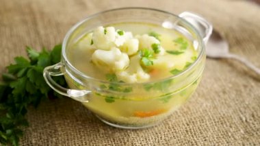 Karnabaharla pişirilmiş tavuk çorbası ve ahşap bir masada bir kasede sebze.