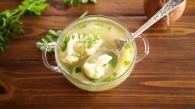 Karnabaharla pişirilmiş tavuk çorbası ve ahşap bir masada bir kasede sebze.