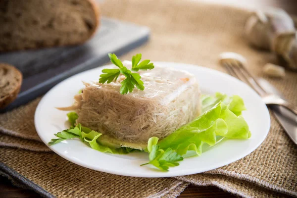 Boiled chicken meat aspic in meat gelatin broth in a plate on a wooden table