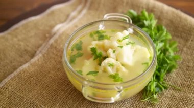 Karnabaharla pişirilmiş tavuk çorbası ve ahşap bir masada bir kasede sebze.