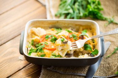 Peynirin altında tavuk filetosu ve mantarla pişirilmiş karnabahar seramik formda, ahşap bir masada..