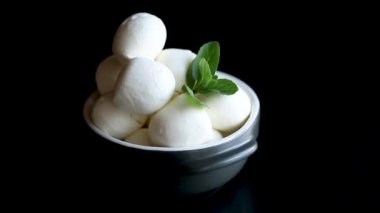 Küçük toplar halinde geleneksel mozzarella seramik bir kasede siyah arkaplanda nane şekeri.