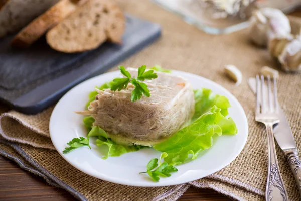 Boiled chicken meat aspic in meat gelatin broth in a plate on a wooden table