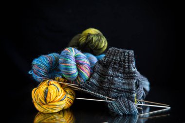 Siyah bir arkaplanda renkli iplikler, örgü iğneleri ve el örgüsü için diğer eşyalar. .