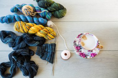 Colored threads, knitting needles and other items for hand knitting, on a light wooden table .