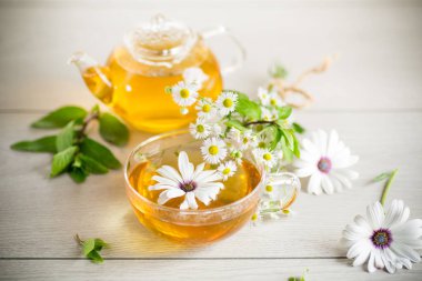 Papatya çiçeği çayı cam fincanda ve çaydanlıkta, açık ahşap bir masada..