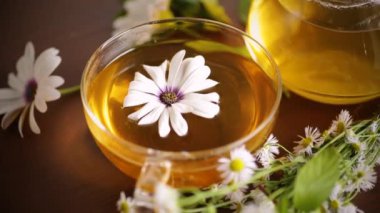 Papatya çiçeği çayı, cam fincanda ve çaydanlıkta, koyu ahşap bir masada..