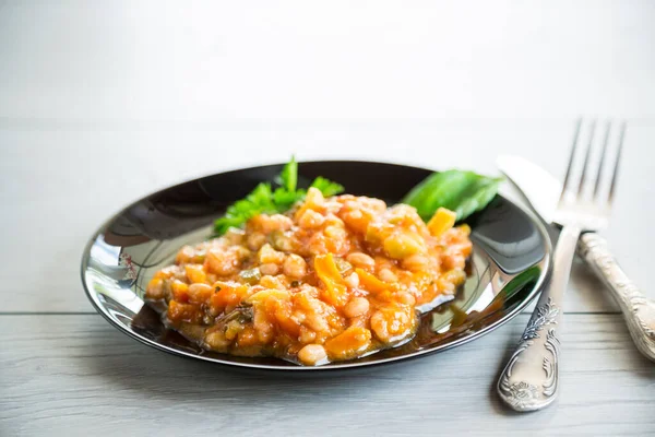 Cooked white beans with zucchini and other vegetables, on a wooden table.