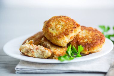 Hafif ahşap bir masada, otlarla dolu bir tabakta kızartılmış balık pirzolası..