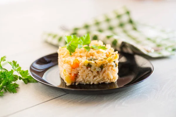 Cooked boiled rice with zucchini, carrots and vegetables in a plate, on a light wooden table.