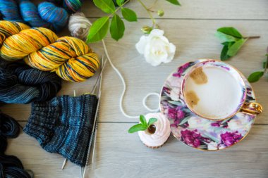 Colored threads, knitting needles and other items for hand knitting, on a light wooden table .