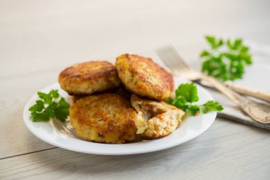 Hafif ahşap bir masada, otlarla dolu bir tabakta kızartılmış balık pirzolası..