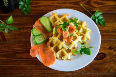 Hafif tuzlu kırmızı balıkla pişirilmiş patates waffle 'ları ve ahşap bir masada, bir tabakta otlar..