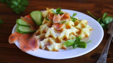 Hafif tuzlu kırmızı balıkla pişirilmiş patates waffle 'ları ve ahşap bir masada serpiştirilmiş otlar..