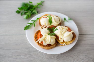 Hamur sandviçlerinde kızartılmış domatesler ve ahşap bir masada otlarla dolu bir tabakta mozzarella..