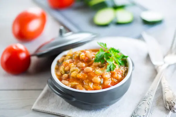Cooked white beans with zucchini and other vegetables, on a wooden table.