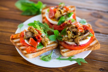 Domatesli sandviç, mozarella ve ahşap bir masada mantarlı kızarmış patlıcan..