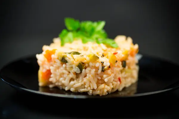 Cooked boiled rice with zucchini, carrots and vegetables in a plate, isolated on a black background.