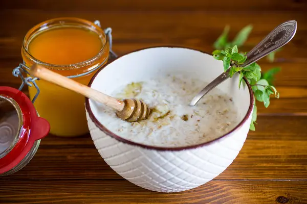 木のテーブルのボウルで朝食のための蜂蜜とミルクオートミールお粥 — ストック写真