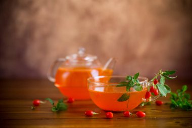 Tahta bir masada, cam bir bardak ve çaydanlıktaki olgun goji üzümlerinden hazırlanmış içecek..