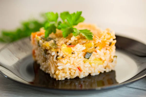 Cooked boiled rice with zucchini, carrots and vegetables in a plate, on a light wooden table.