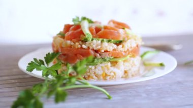 Kaynamış beyaz pirinç, tuzlanmış kırmızı balık, salatalık ve diğer sebzelerle birlikte bir tabakta otlar. Yüksek kaliteli FullHD görüntüler