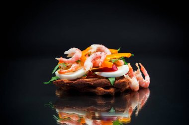 Karides, yumurta, biber ve yeşillikle pişirilmiş sandviç, siyah arka planda izole edilmiş.