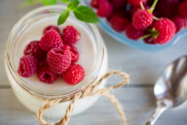 Cam bir kavanozda taze ahududu bulunan ev yapımı yoğurt, açık ahşap bir masada..