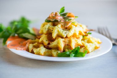 Hafif tuzlu kırmızı balıkla pişirilmiş patates waffle 'ları ve ahşap bir masada, bir tabakta otlar..