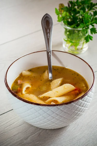 hot vegetable soup with large pasta in a bowl on a wooden table.