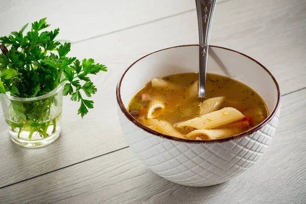 hot vegetable soup with large pasta in a bowl on a wooden table.