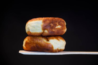 Ahşap bir kürek üzerinde maya hamuruyla dolu kızarmış turtalar, siyah bir arka planda izole edilmiş. Ukrayna yemekleri.