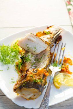 Baharat ve sebzelerle pişirilmiş balık ahşap bir masada bir tabakta..