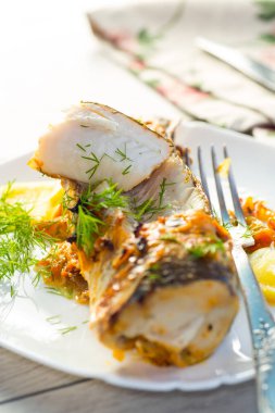 Baharat ve sebzelerle pişirilmiş balık ahşap bir masada bir tabakta..