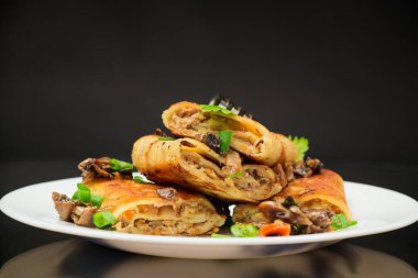 Et, mantar ve siyah arka planda izole edilmiş bir tabağa doldurulmuş ince krepler..