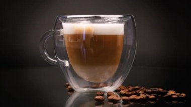 Siyah arka planda, cam bardakta sütlü sıcak kahve.