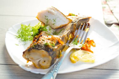 Baharat ve sebzelerle pişirilmiş balık ahşap bir masada bir tabakta..