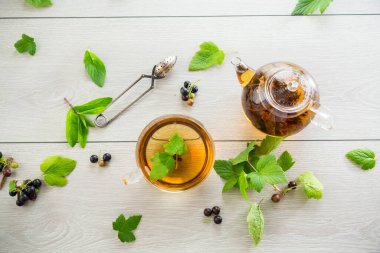 Frenk üzümünden bitki çayı ve bir fincanda böğürtlen ve bir çaydanlıkta, açık ahşap bir masada