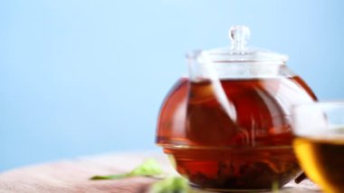 Frenk üzümü yapraklarından bitki çayı ve bir fincanda böğürtlen ve mavi arka planda izole edilmiş bir çaydanlıkta.