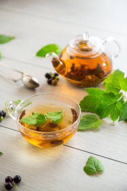 Frenk üzümünden bitki çayı ve bir fincanda böğürtlen ve bir çaydanlıkta, açık ahşap bir masada