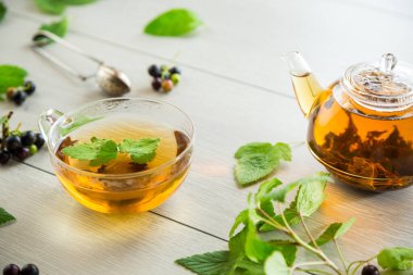 Frenk üzümünden bitki çayı ve bir fincanda böğürtlen ve bir çaydanlıkta, açık ahşap bir masada