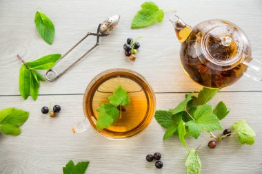Frenk üzümünden bitki çayı ve bir fincanda böğürtlen ve bir çaydanlıkta, açık ahşap bir masada