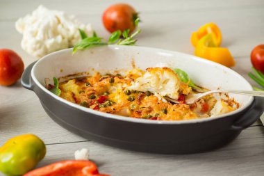 Peynirin altında tatlı biber ve sebzeyle pişirilmiş karnabahar, seramik bir kabın içinde.