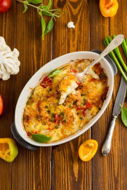 Peynirin altında tatlı biber ve sebzeyle pişirilmiş karnabahar, seramik bir kabın içinde.