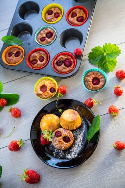 Çilek dolgulu tatlı kremalı kekler, ahşap bir masada bir tabakta..