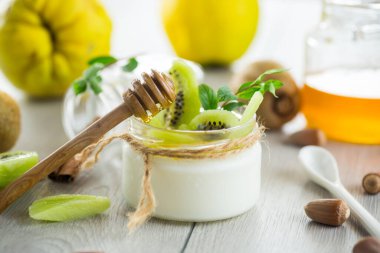 Bal, kivi ve fındıklı cam kavanozda ev yapımı yoğurt. Hafif ahşap bir masada