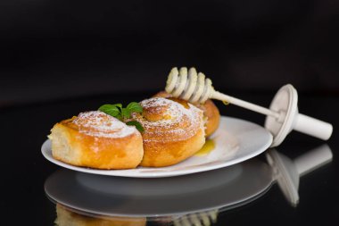 Pişmiş mallar. Süzme peynirli tatlı çörekler ve siyah arka planda izole edilmiş bir tabakta bal. .